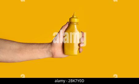 Gros plan du gars du millénaires montrant une bouteille de moutarde sur fond orange, maquette pour le design. Panorama Banque D'Images