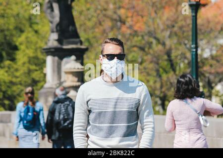 Jeune homme avec lunettes de soleil et masque en tissu cousu photographié sur le pont Charles à Prague, en République tchèque. Arrière-plan flou. Tourisme pendant le coronavirus. COVID-19. Photo horizontale. Banque D'Images