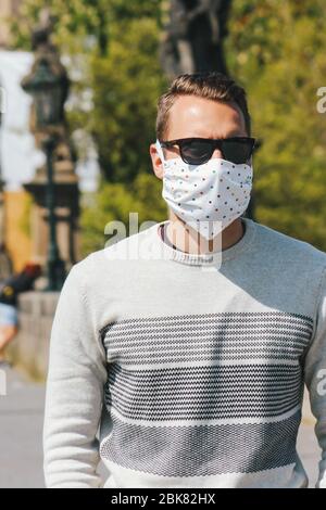 Jeune homme avec lunettes de soleil et masque en tissu cousu photographié sur le pont Charles à Prague, en République tchèque. Arrière-plan flou. Voyager, tourisme pendant coronavirus. COVID-19. Photo verticale. Banque D'Images