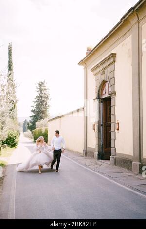 Belle mariée et marié courant main dans la main à l'extérieur de la vieille villa en Italie, en Toscane, près de Florence. Banque D'Images