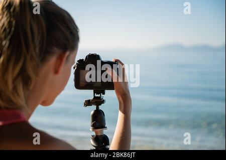 Au-dessus de l'épaule de la photographe féminine qui organise les réglages de l'appareil photo, elle se prépare à prendre de belles photos de mer et de paysage le matin. Banque D'Images