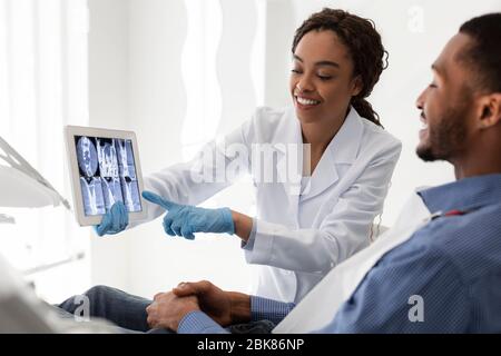 Dentiste féminin africain souriant montrant des rayons X sur les dents du patient Banque D'Images