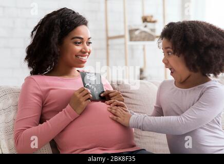 Bonne attente pour une femme noire montrant une sonographie à une petite fille excitée Banque D'Images