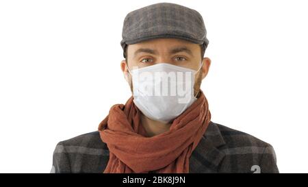 Beau jeune homme européen en manteau tendance portant un masque de protection jetable sur fond blanc. Banque D'Images