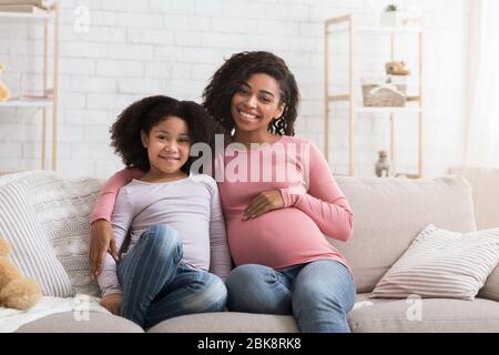 Bonne femme africaine enceinte et sa petite fille se détendant à la maison Banque D'Images