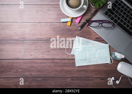 masque chirurgical et flacon de solution désinfectante ou gel d'alcool avec ordinateur portable et café sur fond de bois ancien, travail à la maison et concept covid-19 Banque D'Images