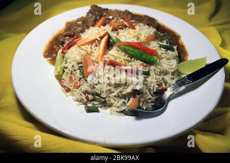 Riz frit aux légumes avec poulet au Chili sur une plaque blanche isolée sur un chiffon jaune. Vue de dessus. Le poulet au Chili est un plat indo-chinois populaire Banque D'Images