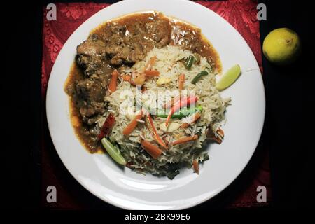 Riz frit aux légumes et poulet au piment sur une assiette blanche avec citron et piment isolés sur fond noir. Vue de dessus. Le poulet au Chili est un indo-chine populaire Banque D'Images