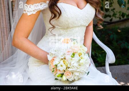 Mariée assise tenant un beau bouquet de mariage de roses et d'eustoma. Banque D'Images