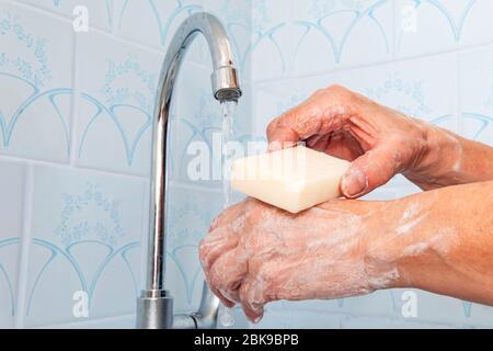 femme tient dans ses mains du savon sur lequel l'eau coule du robinet de métal sur fond bleu. Prévention des maladies virales et des épidémies. Combat contre le coronavi Banque D'Images