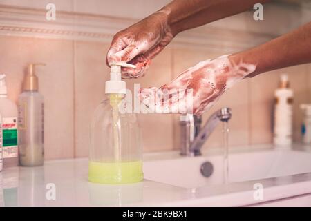 Se laver les mains avec du savon sous l'eau courante. Une femme afro-américaine se lave les mains, appuie sur la bouteille avec du savon et de l'eau. Banque D'Images