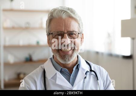 Professionnel souriant homme plus âgé médecin regardant l'appareil photo, gros plan portrait Banque D'Images