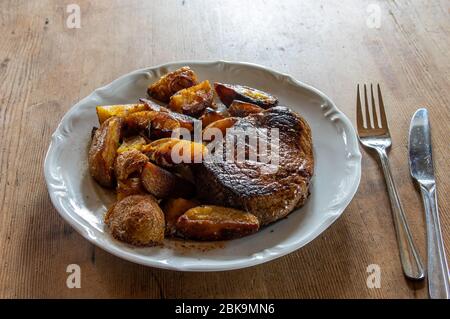 Steak de bœuf Black Angus avec quartiers de pommes de terre sur une assiette blanche sur une table en bois sombre avec fourchette et couteau Banque D'Images