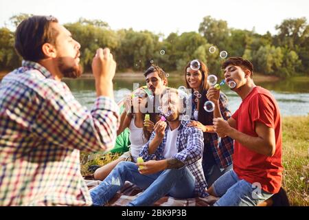 Les jeunes font des bulles de savon tout en étant assis sur l'herbe sur la nature. Banque D'Images