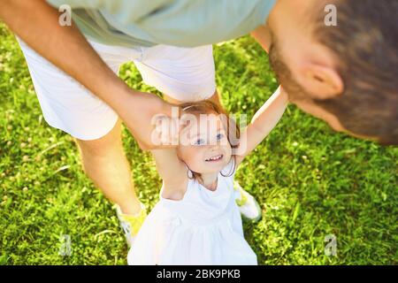 Fête des pères. Le père joue avec sa fille sur l'herbe dans le parc d'été une journée ensoleillée. Banque D'Images