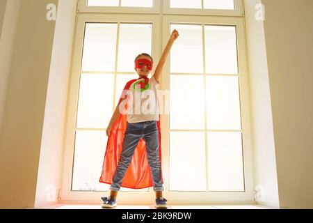 Enfant super héros.Kid sourire jouant un super héros s'amuser dans une chambre avec une fenêtre. Banque D'Images