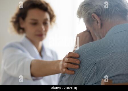 Médecin de femme touchant l'épaule réconfortant patient senior bouleversé, la proximité Banque D'Images