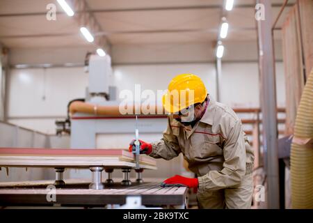 Beau homme mûr dans le matériel de protection de travail travaillant dans l'usine de meubles Banque D'Images