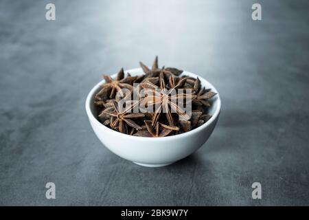 Étoiles anis dans un bol en porcelaine blanche sur fond de pierre, béton. Banque D'Images