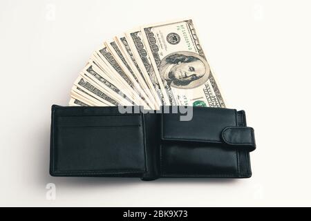 Un portefeuille noir avec des dollars en lui sur un fond blanc. Les factures de cent dollars sont à moitié sorties et arrangées en ventilateur. Image couleur à contraste intégral. Banque D'Images