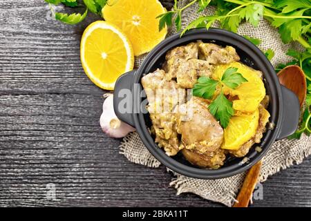 Poulet rasé avec des oranges, de la crème aigre, de la sauce soja et des herbes de Provence dans une petite poêle sur la serviette de sauge, la cuillère et le persil sur le dos de planche en bois Banque D'Images