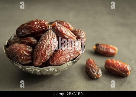 Fruits de date crus prêts à manger dans un bol d'argent sur fond de béton. Une cuisine traditionnelle, délicieuse et saine pour le ramadan. Banque D'Images