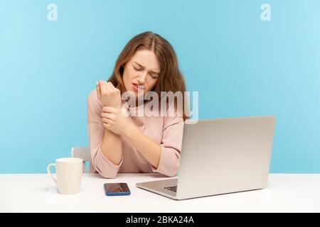 Employé de bureau de femme malade fatigué assis sur le lieu de travail avec ordinateur portable et tenant le poignet douloureux, souffrant de douleur dans la main blessée, syndrome de tunnel carpien. indo Banque D'Images