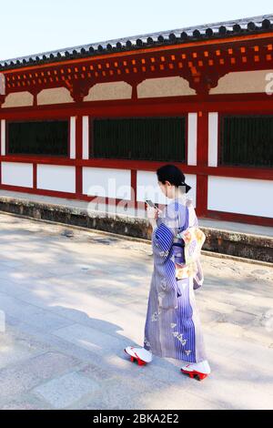 Une japonaise en kimono qui vérifie son smartphone tout en marchant dans un bâtiment traditionnel Banque D'Images