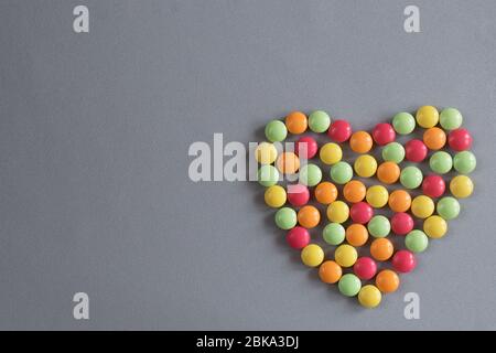 forme de coeur de comprimés multicolores de dragées sur fond gris tissé Banque D'Images