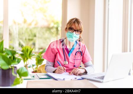 Portrait de la femme médecin portant un masque pour la prévention tout en travaillant sur un ordinateur portable au bureau du médecin. Banque D'Images