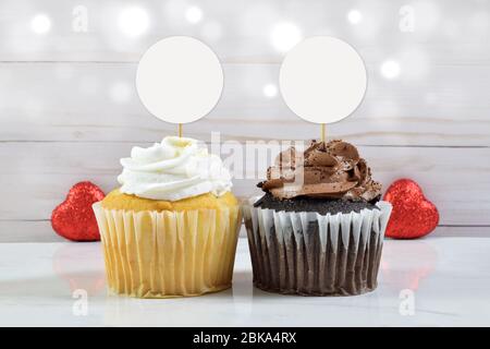 Un chocolat gourmand et un cupcake à la vanille reposent entre deux coeurs rouges scintillants dans cette maquette de topper de Saint-Valentin. Banque D'Images