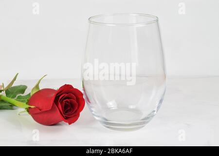 Un verre de vin sans tige frise romantisme à côté d'une longue rose rouge à tige. Banque D'Images