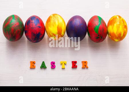 Lettres en bois multicolores composant les mots Happy easter et œufs colorés décoratifs sur fond blanc avec espace de copie. Banque D'Images