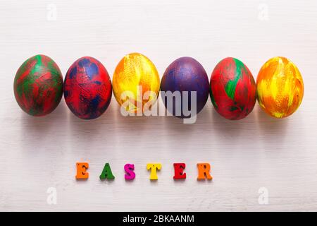 Lettres en bois multicolores composant les mots Happy easter et œufs colorés décoratifs sur fond blanc. Banque D'Images