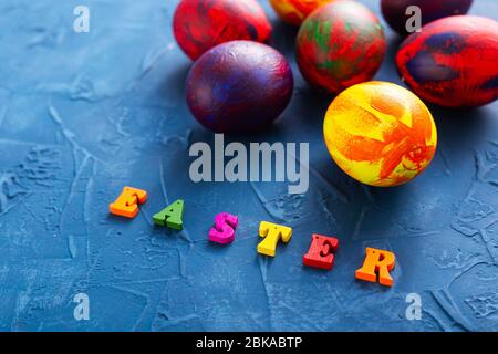 Lettres en bois multicolores représentant les mots joyeuses pâques et des œufs décoratifs colorés sur un fond bleu. Banque D'Images