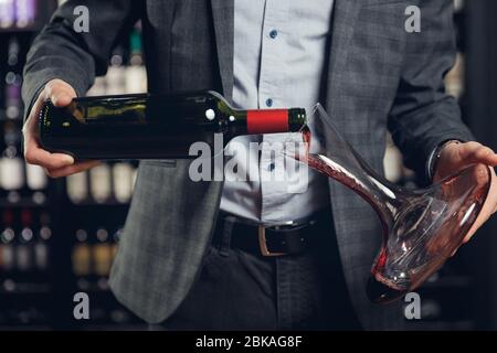 L'homme sommelier verse le vin rouge dans un décanteur pour l'aération du goût et de l'arôme Banque D'Images