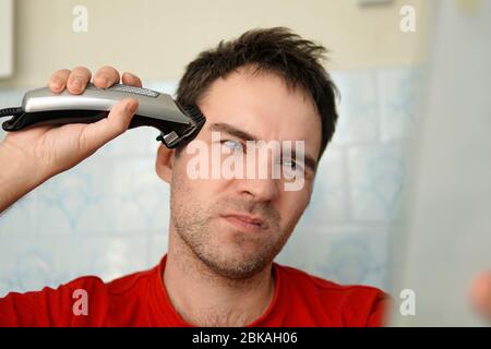 Un homme coupe ses cheveux sur la tête avec un rasoir électrique. Nettoyez-vous seul. Vous souffrez de la tonte des cheveux Banque D'Images