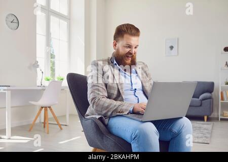 Travailler en ligne au bureau à domicile. Un homme de graisse drôle travaille avec un ordinateur portable dans la chambre d'appartement.