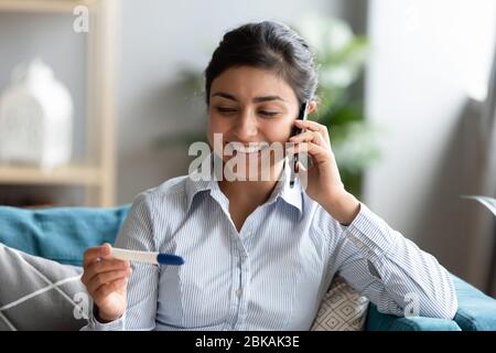 Heureuse femme indienne millénaire tenant un test de grossesse positif, partageant des nouvelles. Banque D'Images