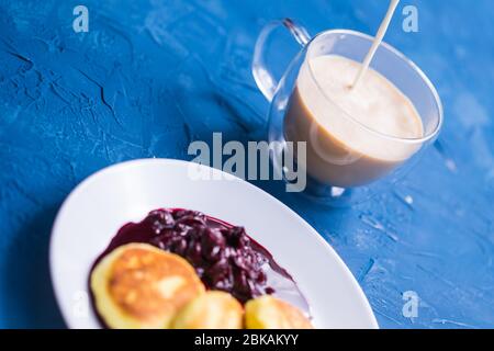 Crêpes au fromage cottage avec confiture de cerises, vue rapprochée, vue de dessus. Verser du café dans une tasse. Banque D'Images