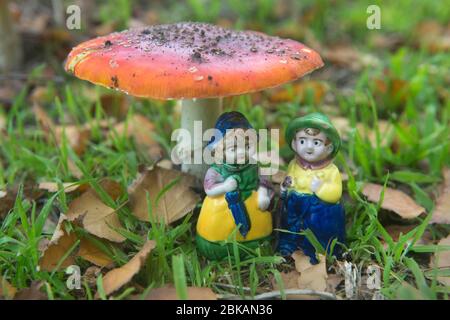 Deux poupées de chine sous un tabouret de crapaud parmi l'herbe et les feuilles Banque D'Images