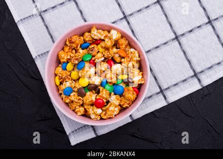 Boutons de chocolat colorés et popcorn doré dans un bol sur la serviette. Banque D'Images