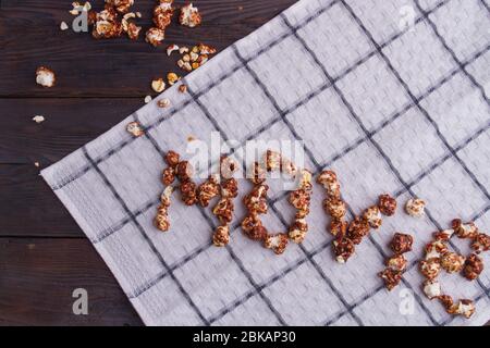 Grains de popcorn au chocolat disposés en mots de cinéma sur fond de serviette blanc. Banque D'Images