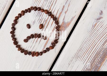 Le visage sourit de grains de café est malheureux sur le bois blanc. Banque D'Images