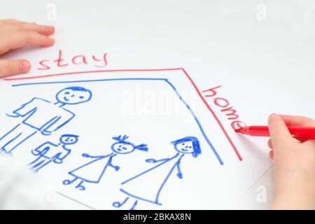 L'enfant écrit des mots rester à la maison avec la famille heureuse dessinée sur la feuille blanche de papier à la maison. Enfants créativité. Banque D'Images