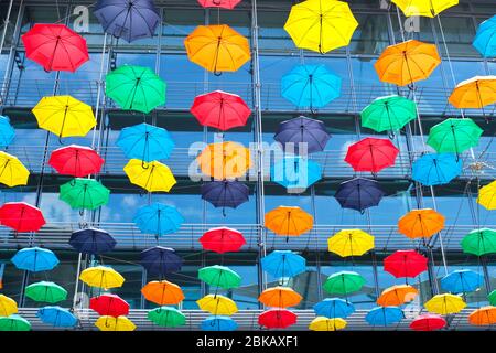 grande quantité de parasols ouverts multicolores suspendus en plein air avec toile de fond de bâtiment en verre Banque D'Images