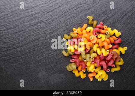 Pâtes spirales multicolores éparpillées sur un fond d'ardoise noire pour le texte de l'espace. Banque D'Images