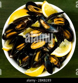 Bol de moules fraîches colorées fraîchement cuites à la vapeur dans des coquillages ouverts avec des Wedges au citron, sur UN plateau de table vert sans personne Banque D'Images