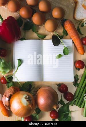 Ordinateur portable ouvert entouré de légumes. Liste d'épicerie avec des légumes autour. Il y a une liste de magasins avec des légumes qui l'entourent. Il y a des épiceries Banque D'Images