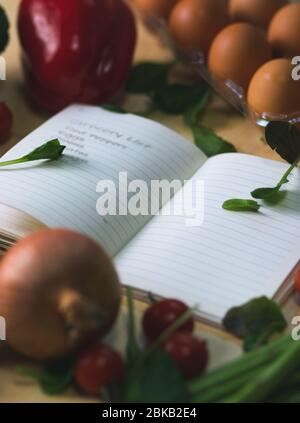 Ordinateur portable ouvert entouré de légumes. Liste d'épicerie avec des légumes autour. Il y a une liste de magasins avec des légumes qui l'entourent. Il y a des épiceries Banque D'Images